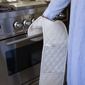 woman opening a silver oven wearing a cream coloured double oven mitt