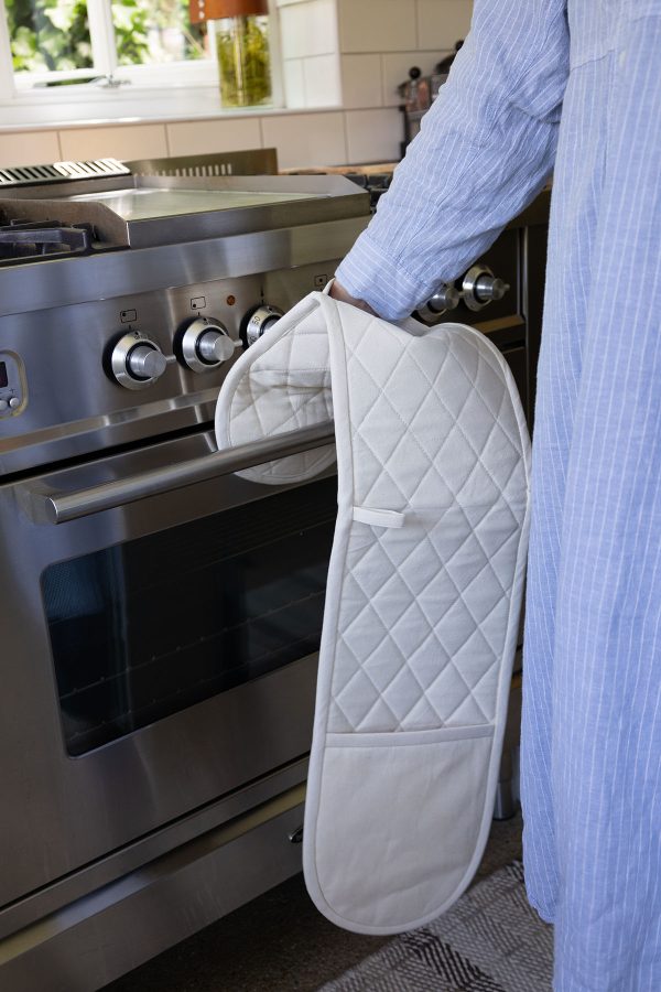 woman opening a silver oven wearing a cream coloured double oven mitt